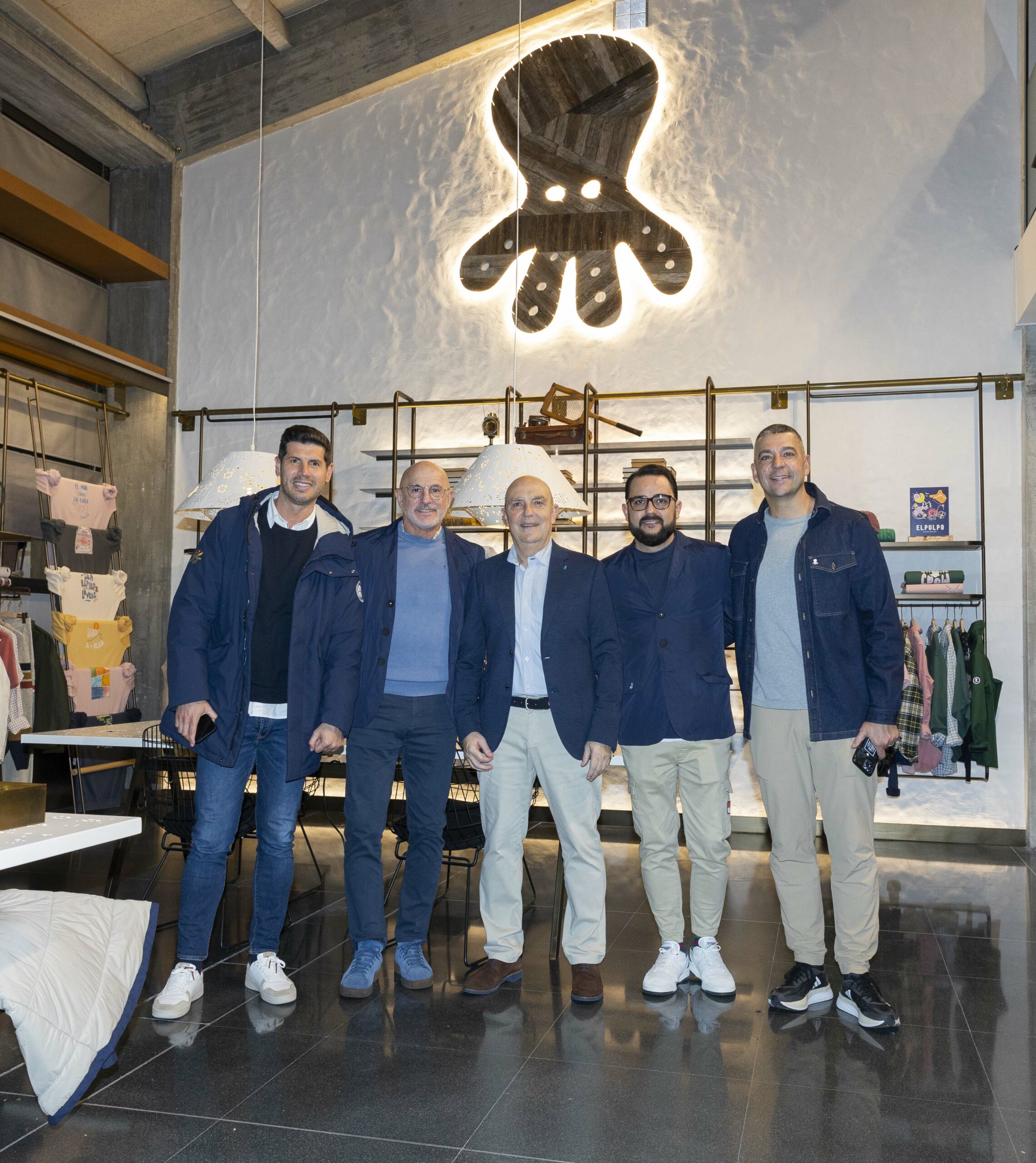 El reconocido grupo textil gallego elPulpo,que aglutina las firmas de moda elPulpo y Nanos y la agencia de representación multimarca CHC Brands, celebró hoy la inauguración de su nueva sede central en Bergondo, A Coruña. Esta moderna instalación supone el inicio de una nueva era de implantación de avanzadas mejoras tecnológicas fundamentales para el desarrollo y crecimiento del grupo textil, con el objetivo de consolidarse como un referente de responsabilidad y sostenibilidad dentro y fuera de nuestras fronteras. Además, los nuevos headquarters de elPulpo le permitirán ser motor para generación de empleo, la formación del talento y un ejemplo en buenas prácticas en materia sostenible y de RSC. Un proyecto que, en definitiva, destaca por la innovación y la profesionalización en todas sus áreas. Alfonso Rueda, presidente de la Xunta de Galicia, ha sido el encargado de inaugurar las oficinas centrales de elPulpo, en donde puso en valor la moda gallega como uno de los bastiones que mejor representa el impulso de la Comunidad, destacando la trayectoria de la firma elPulpo que, en palabras de Rueda, es ya un referente en el mercado autonómico y nacional, un éxito alcanzado gracias a su apuesta por la sostenibilidad y a su marcado carácter gallego. Por su parte, José A. Chacón, fundador de la marca gallega afirmó que “Este proyecto supondrá un antes y un después para el Grupo, puesto que gracias a las nuevas instalaciones podremos tener capacidad de control total del proceso de producción y de toda de la cadena de valor. Hemos hecho una firme apuesta por la profesionalización de la compañía, invertido en programas tecnológicos y de diseño digital, y continuamos con nuestro compromiso con la sostenibilidad, que supone el corazón y la razón de ser de nuestro proyecto.Nuestro sueño es posicionarnos como referentes textiles gallegos en el mundo y ser ejemplo para otras pymes de nuestra comunidad, siempre generando recursos desde Galicia, donde están nuestras raíces”. La apertura de esta nueva sede es el preludio de un ambicioso plan de expansión e internacionalización a corto plazo, con el foco puesto en la apertura de mercados europeos y latinoamericanos. La nueva sede del Grupo para albergar el proyecto textil de elPulpo y Nanosdestaca a nivel logístico y cuenta con un total de 3.000 metros cuadrados. El diseño refleja la esencia y el ADN de elPulpo con un showroom donde todo el mobiliario es sostenible realizado en madera de batea y hierro forjado artesanalmente. El objetivo es que la sede sea 100% sostenible en 2025. Entre los principales objetivos del grupo en la nueva sede para 2024destacan digitalización y modernización; la inversión en talento humano; la implantación de un sistema ERP para optimizar recursos y aumentar la productividad; la creación de un departamento de Diseño Avanzado con técnicas de diseño digital en 3D; la adquisición de equipos avanzados; la adaptación a los objetivos sostenibles de la compañía como eficiencia energética, apuesta por recursos naturales, reciclaje, etc.; y mejora en la calidad de trabajo y conciliación con  modalidades híbridas de teletrabajo y trabajo presencial. elPulpo 2005 fue el año en que se gestó el proyecto de elPulpo, una fashion brand con espíritu atlántico en el que la sostenibilidad, el océano, el respeto por el medio ambiente y la frescura de las rías gallegas se convirtieron en nuestras señas de identidad.  elPulpo es una empresa 100% gallega, respaldada y dirigida por el equipo de José A. y Jorge Chacón, cuya trayectoria profesional está avalada por más de 35 años en el sector textil, y donde la apuesta por Galicia como punto de origen es la razón de ser y eje estratégico.